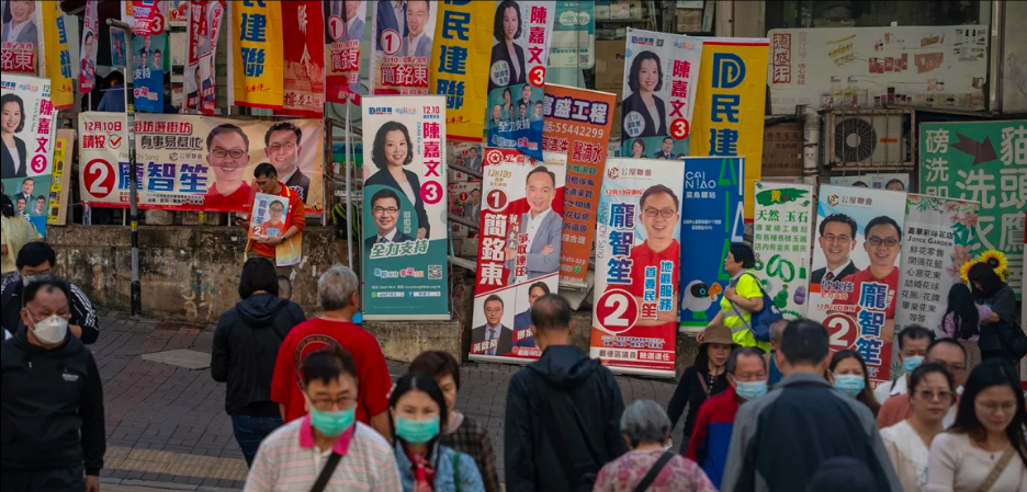 Residents crossing the street in front of a wall of campaign posters for the district council elections in Hong Kong, December 10, 2023. Vernon Yuen/NurPhoto/Getty Images